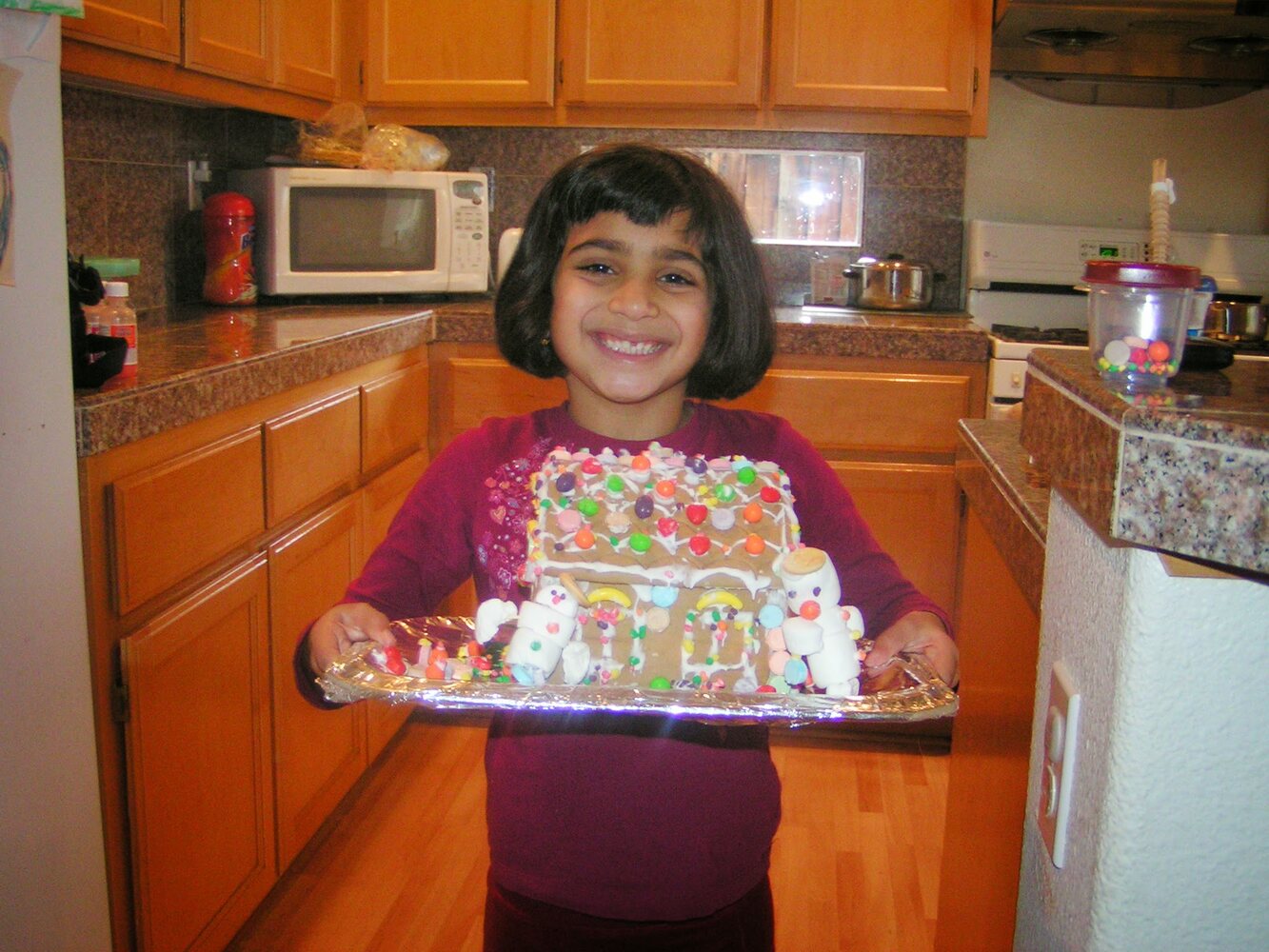 Young Shailee holding a decorated gingerbread house